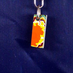 Colorful, rectangular keychain against dark fabric background.