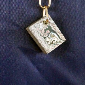 Metal pendant with swirling patterns on fabric.