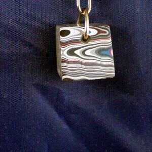 Multicolored layered cube pendant on blue background.