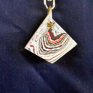 Colorful geometric pendant on dark fabric background.