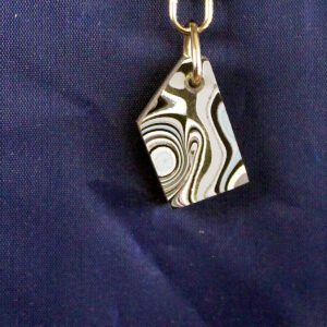 Abstract patterned pendant on blue fabric background.