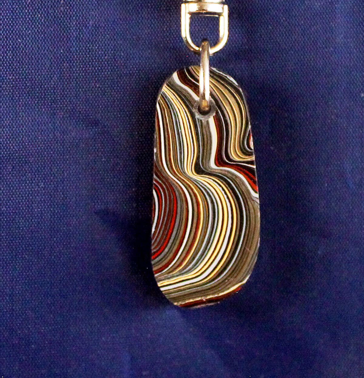 Striped pendant with metal clasp on blue background.