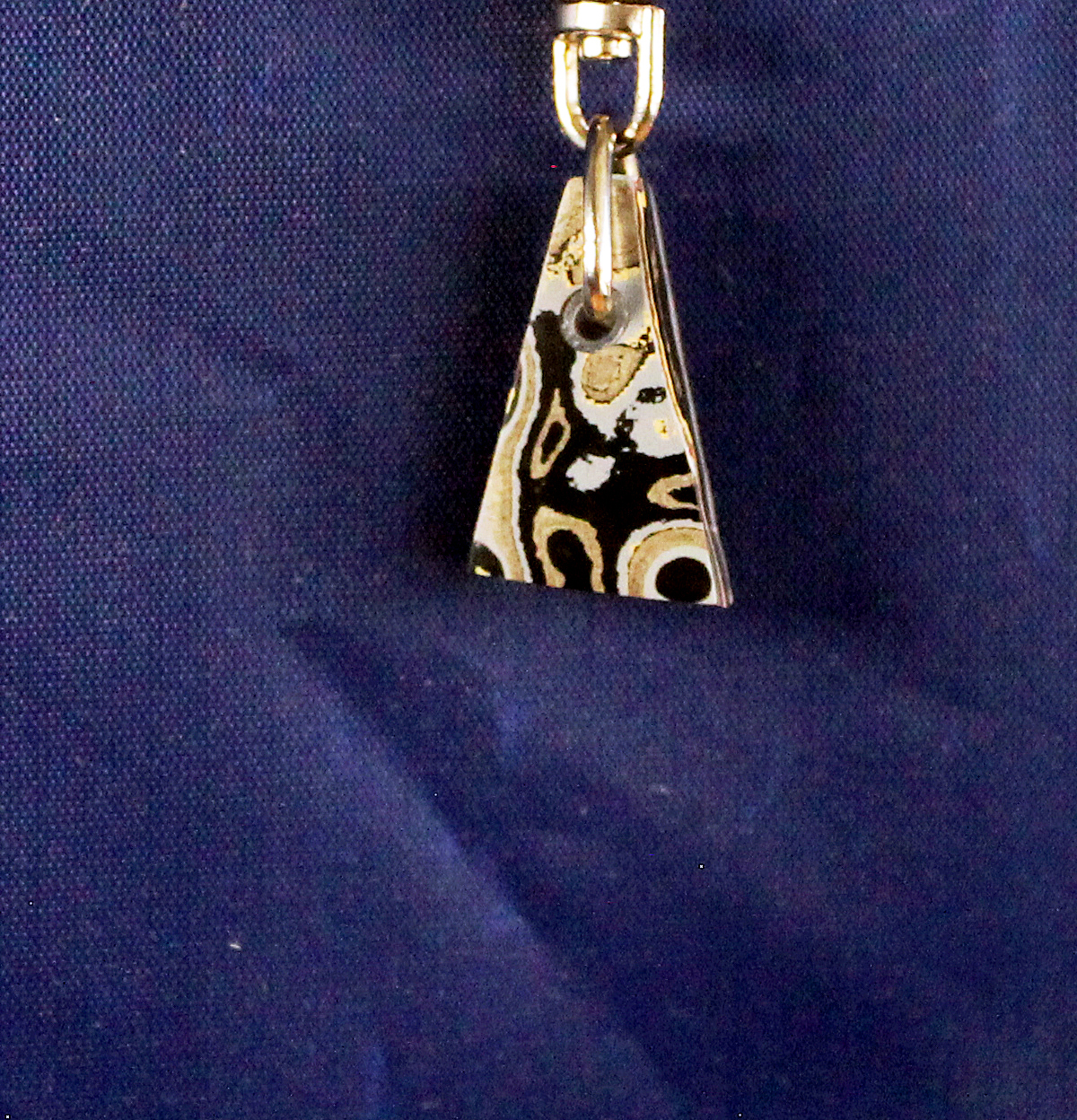 Triangular patterned pendant on blue fabric.