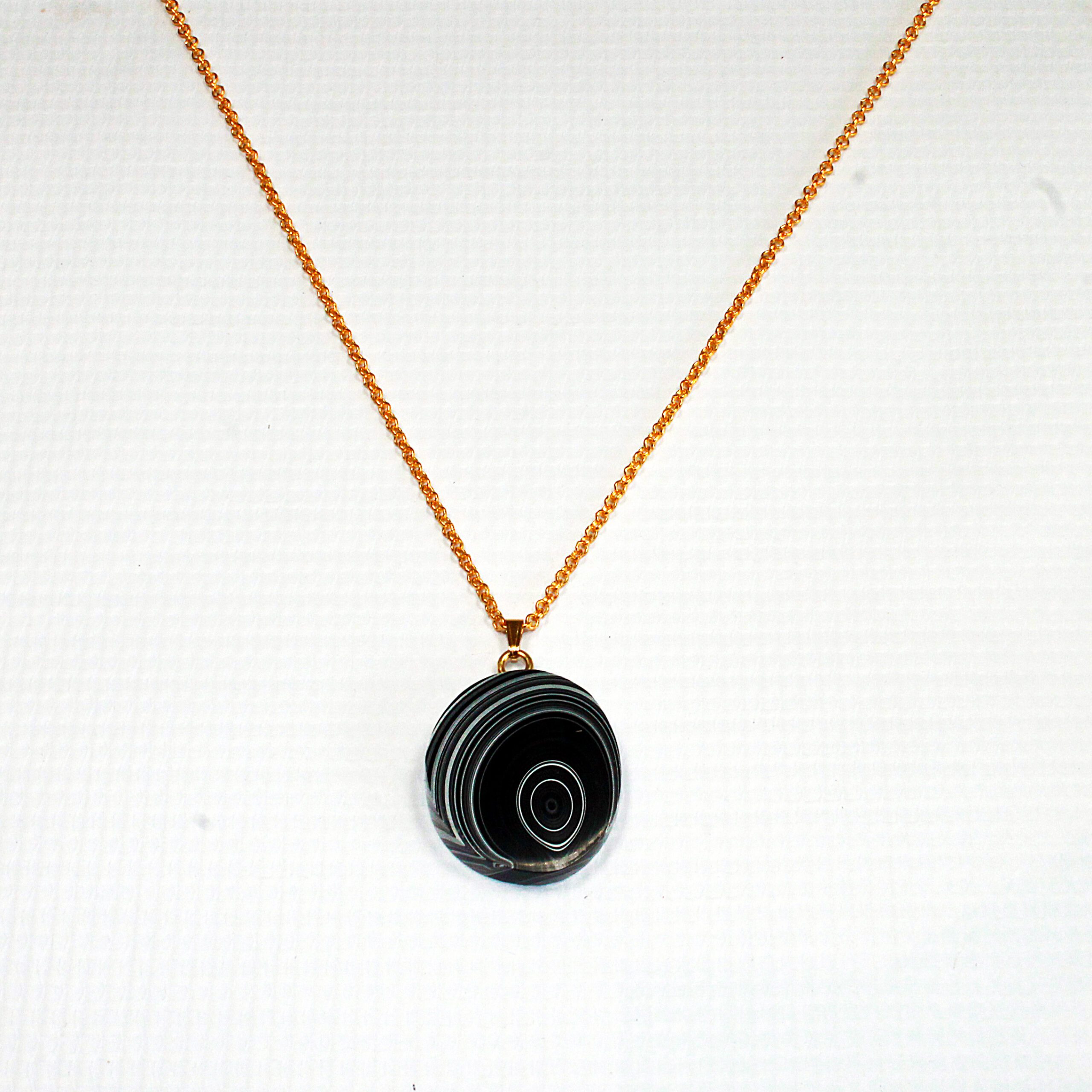 Gold necklace with circular black pendant.