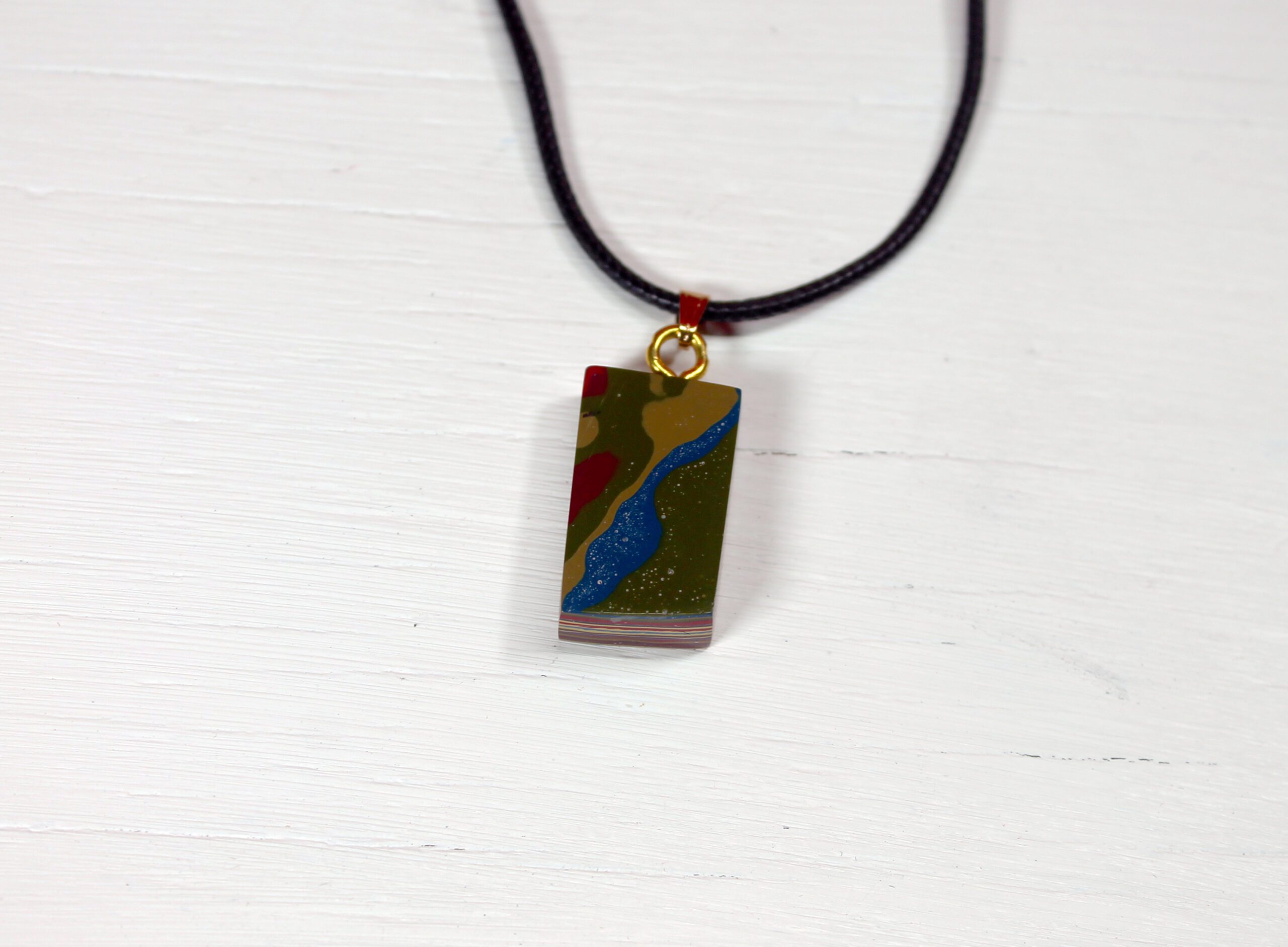 Colorful rectangular pendant on black cord.