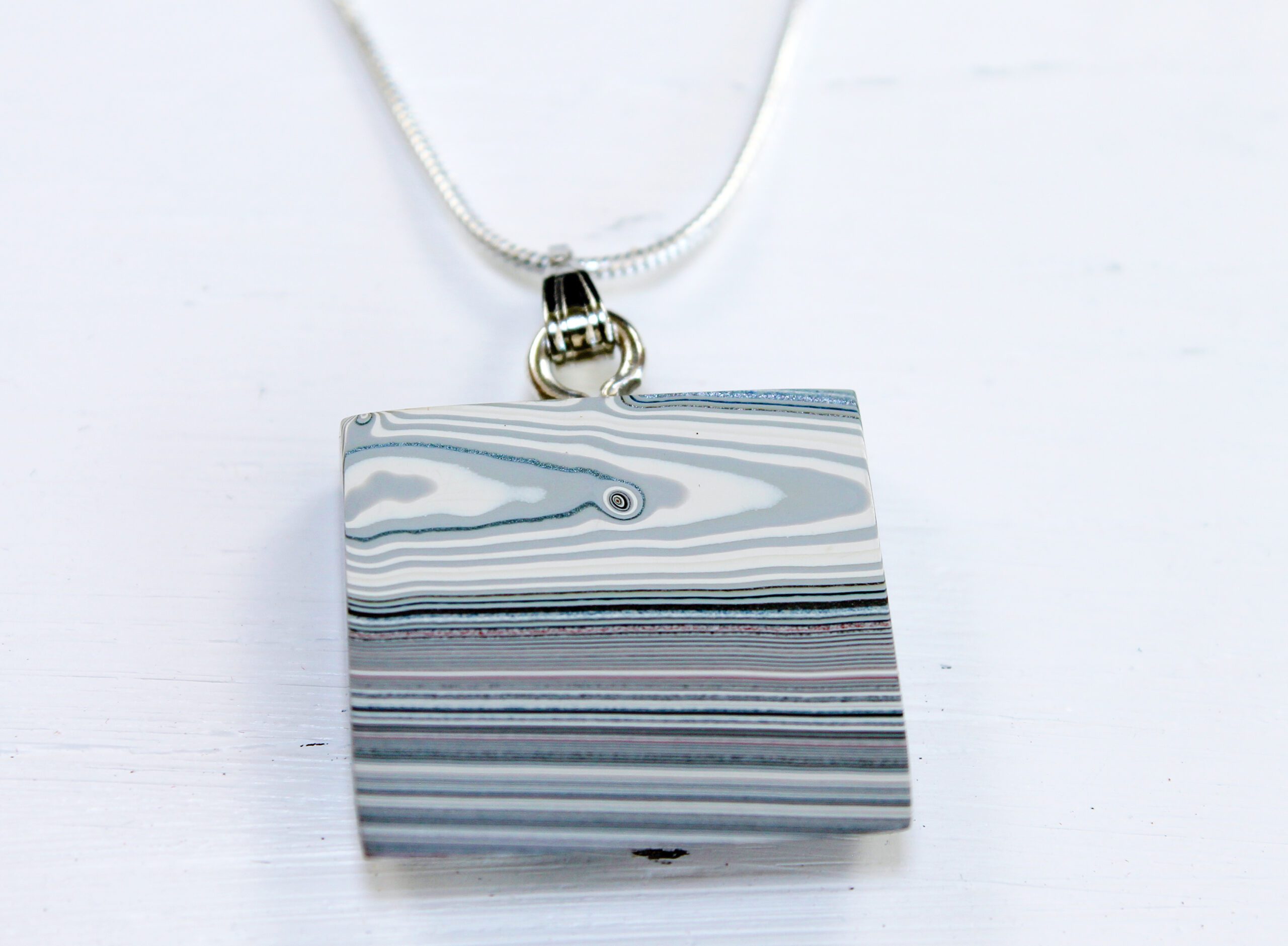 Striped pendant necklace on light background.