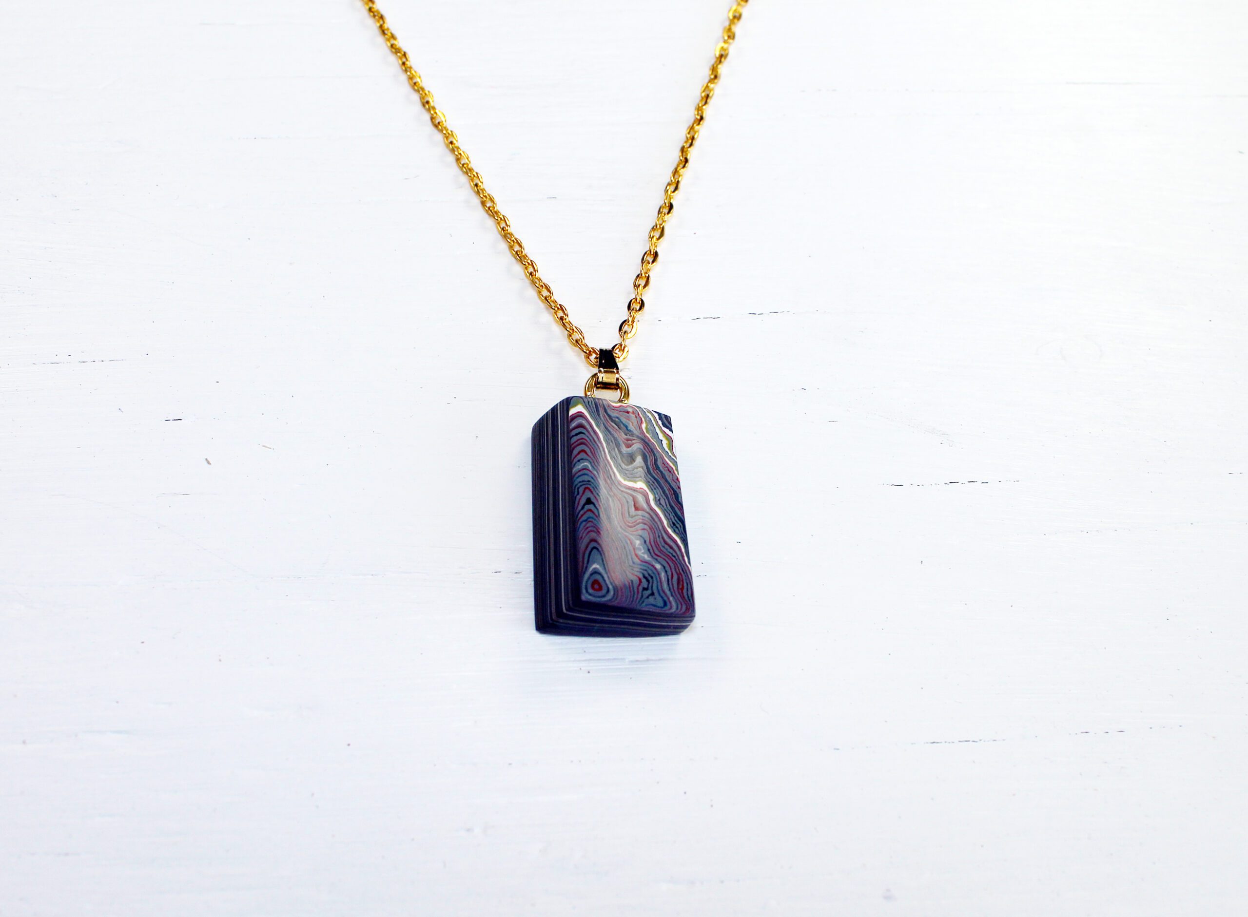 Pendant on gold chain against white background.