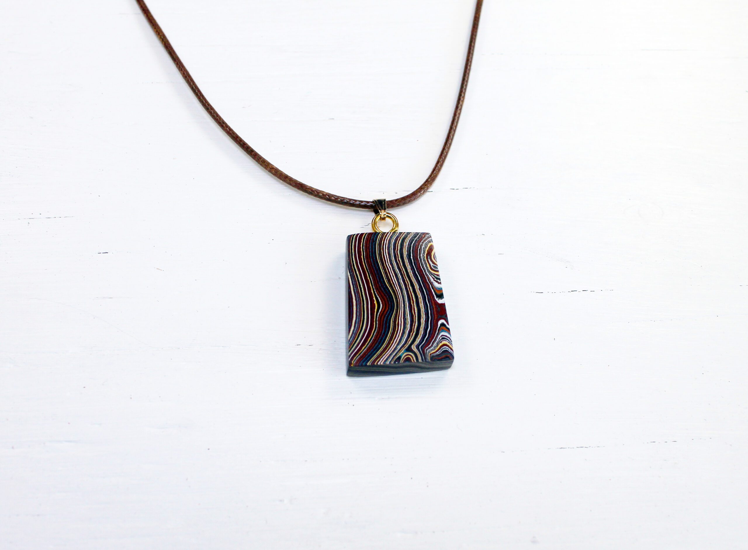 Rectangular pendant on a brown cord necklace.