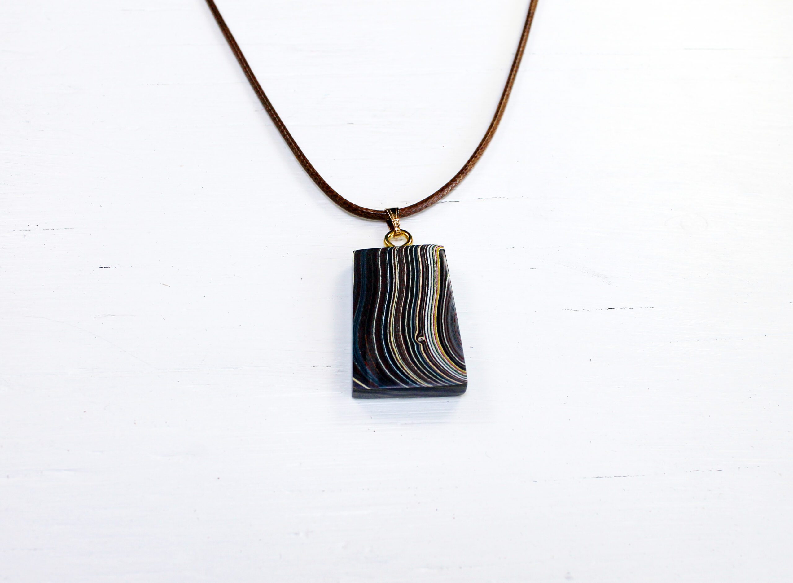 Striped pendant on a brown cord necklace.