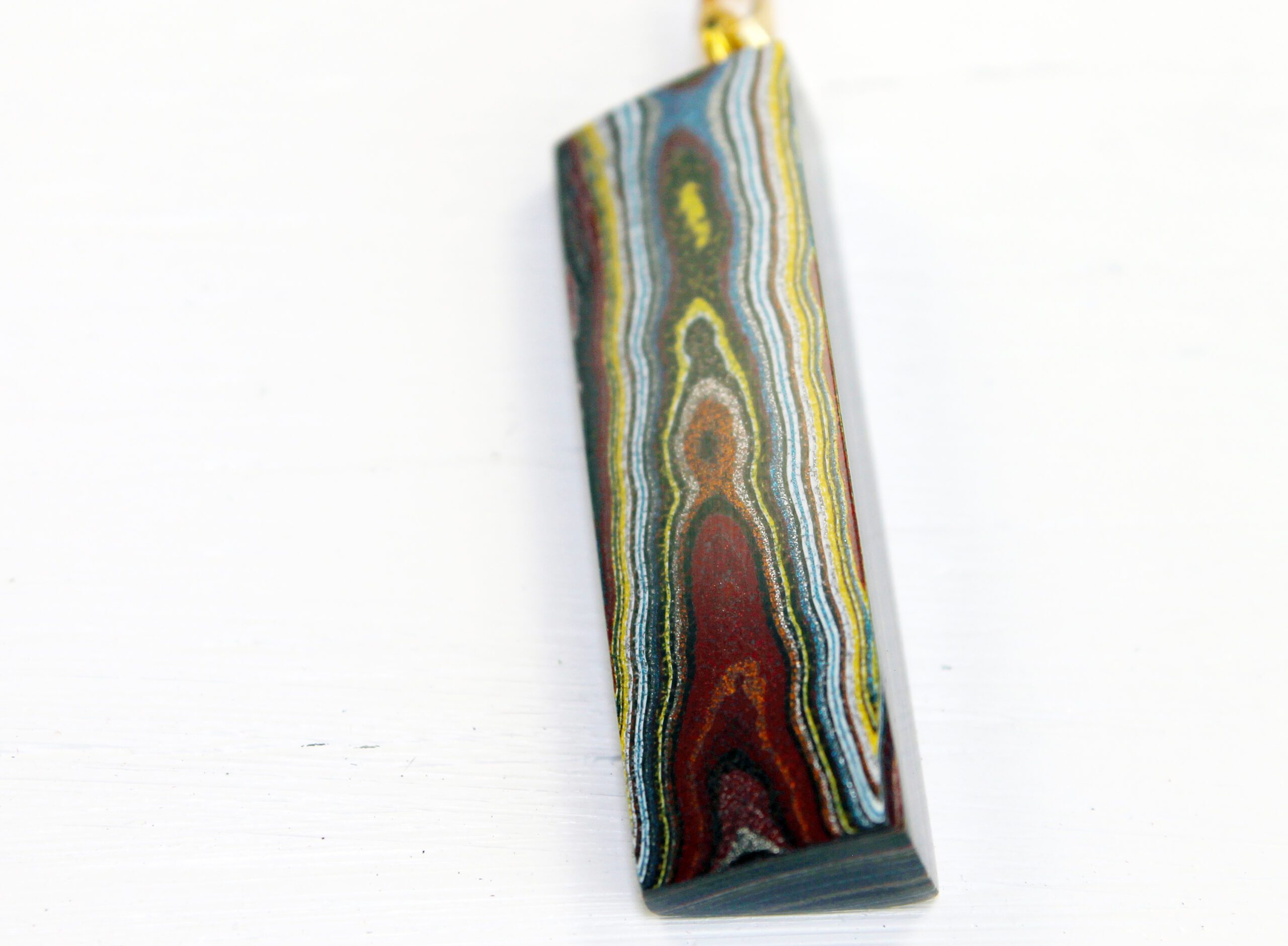 Colorful layered stone pendant on white background.