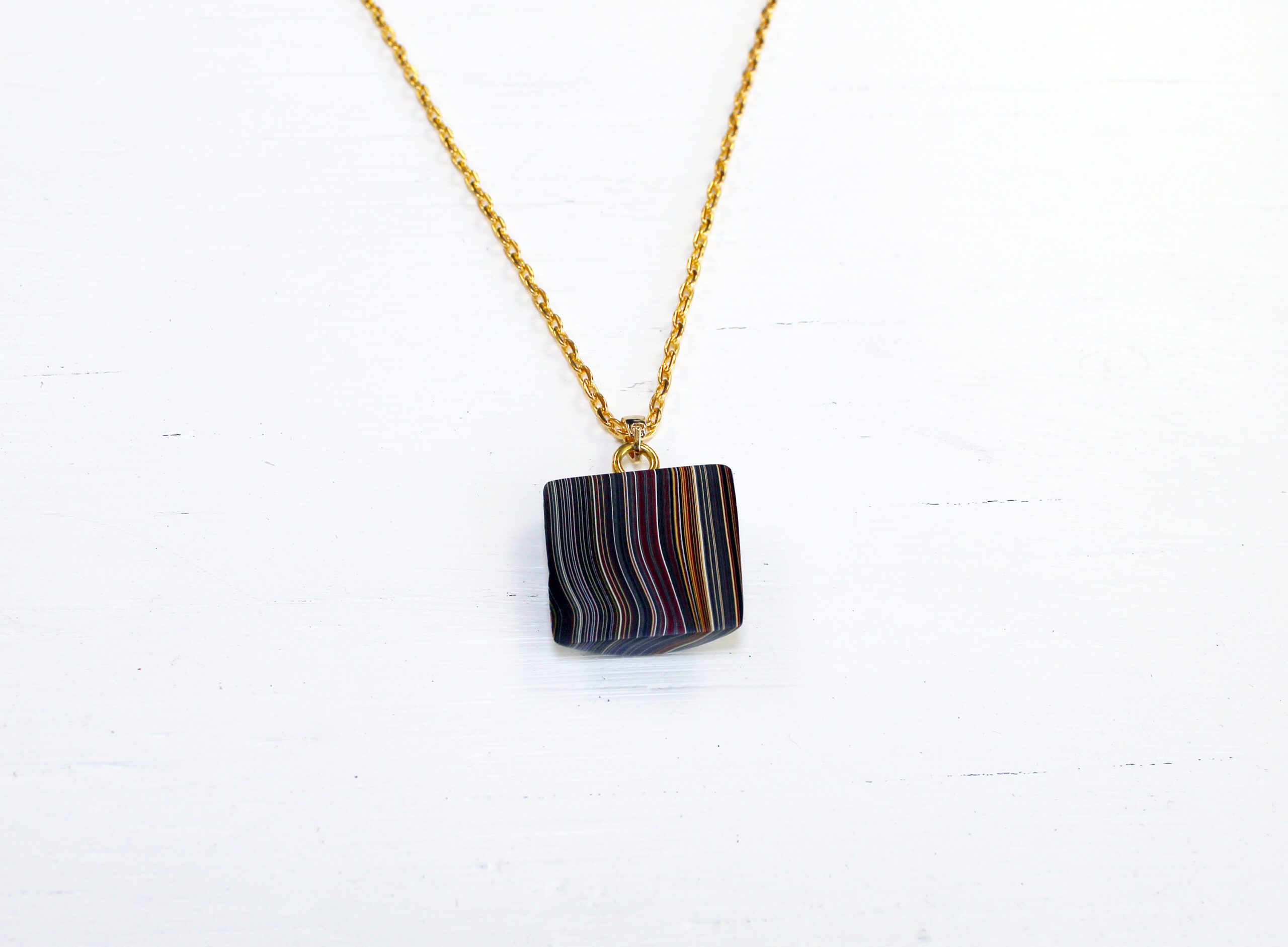 Gold necklace with colorful striped pendant.