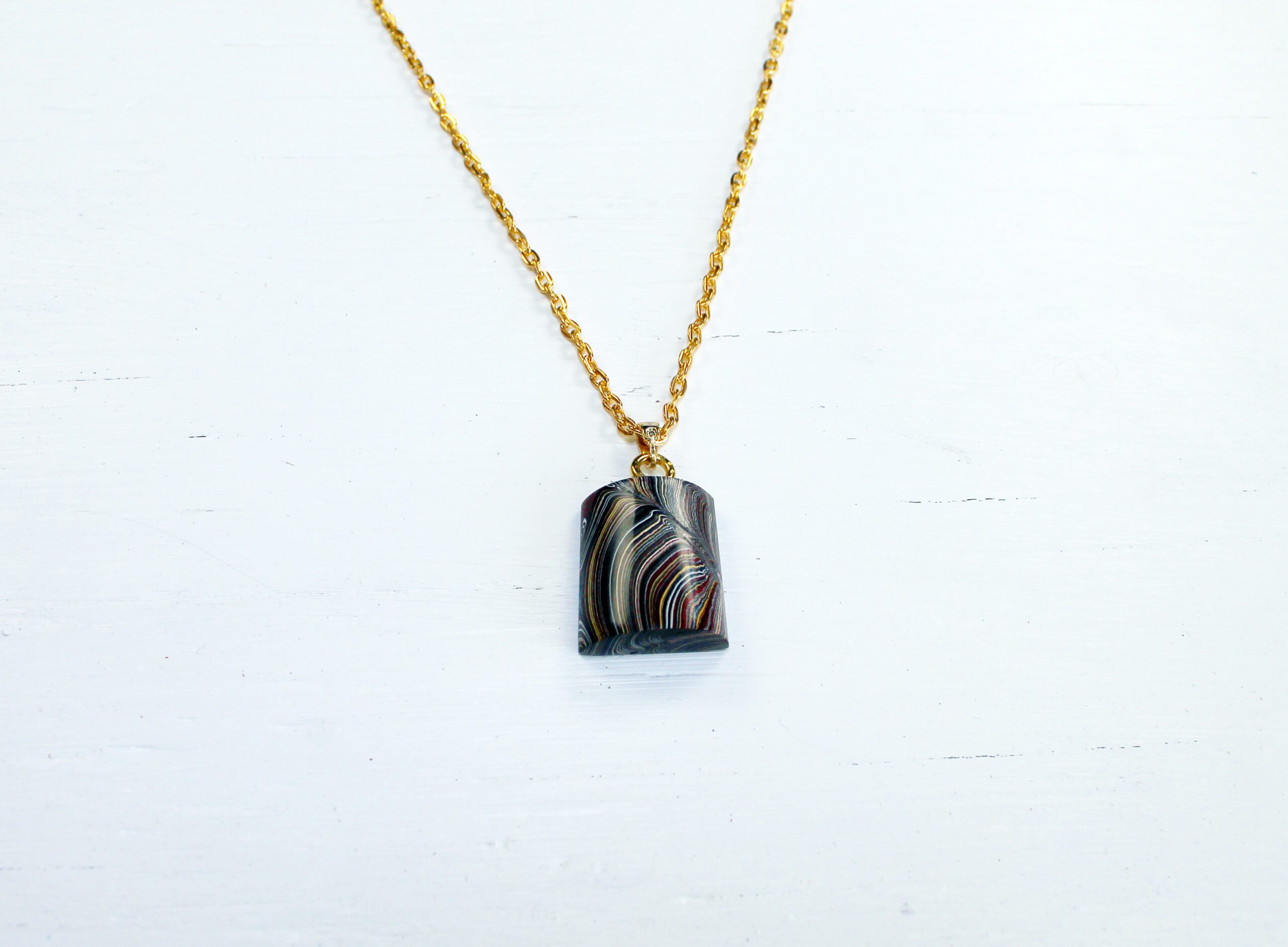 Gold chain with a colorful pendant.
