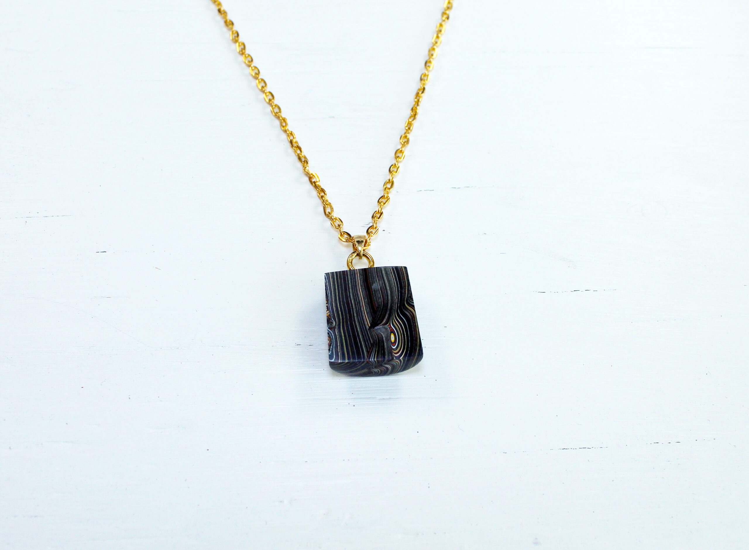 Gold chain with dark pendant on white.