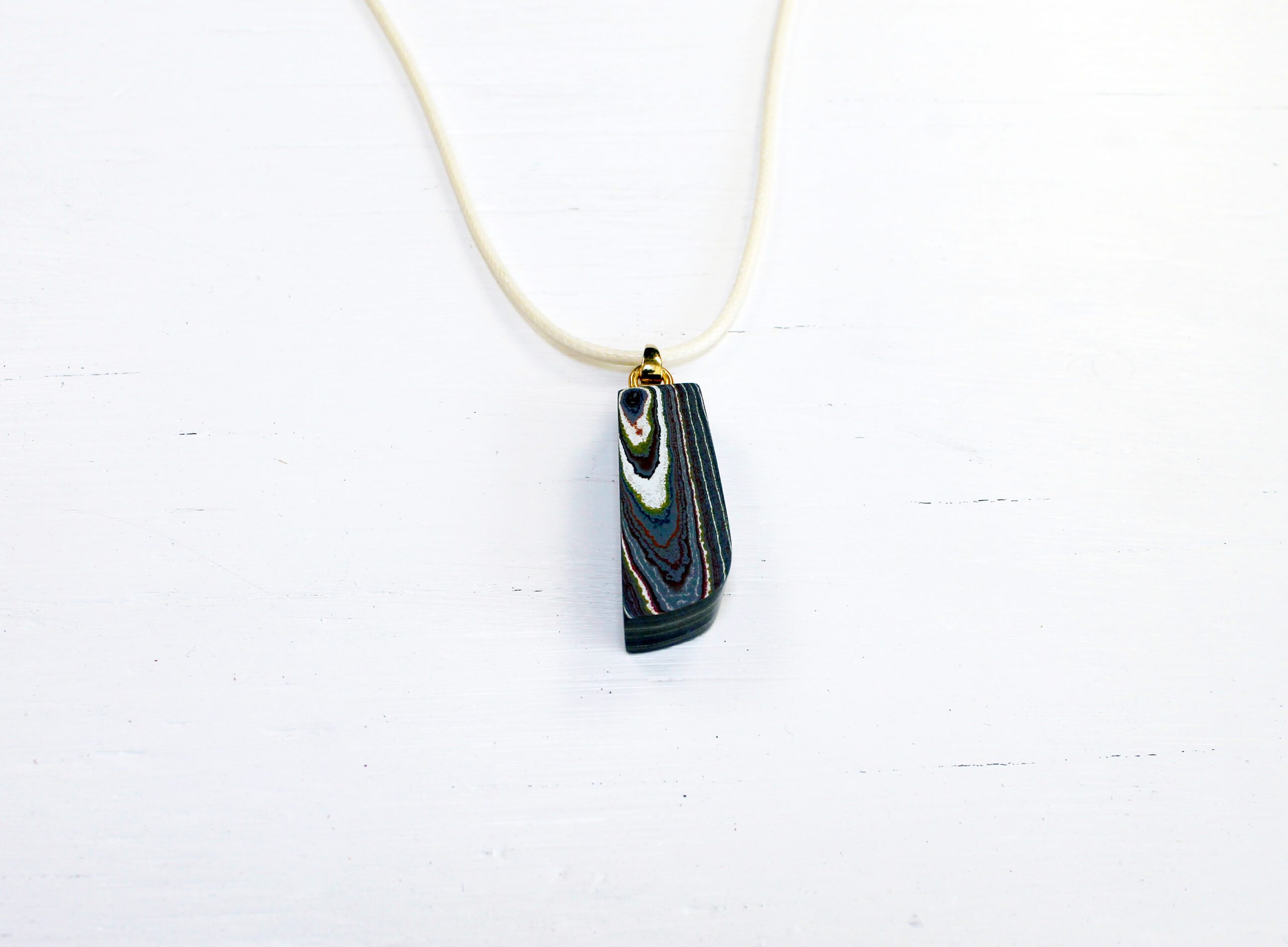 Colorful stone pendant on white necklace.